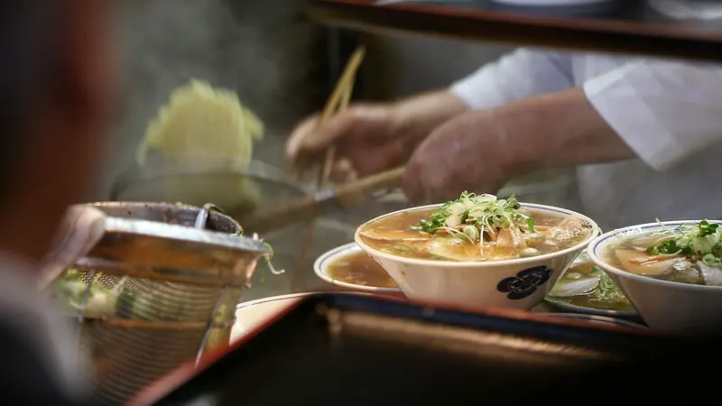 Zwei Schalen Nudelsuppe, die in der offenen Küche angerichtet werden