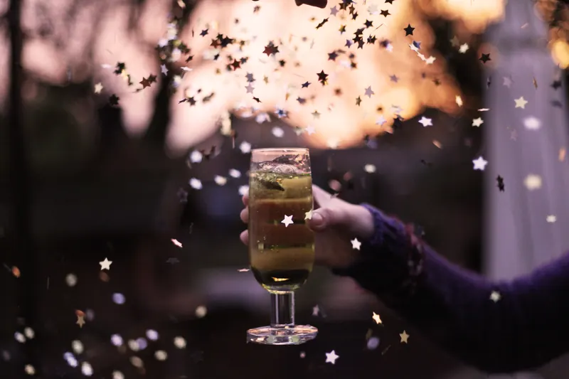 Hand mit einem Glas Bier vor funkelndem Lichterhintergrund