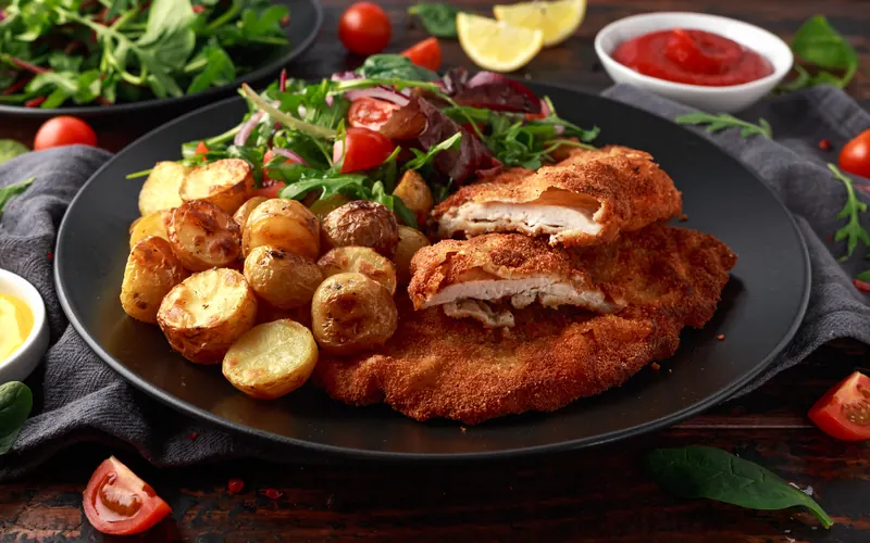 Schnitzel mit Röstkartoffeln und Rucola auf einem dunklen Teller